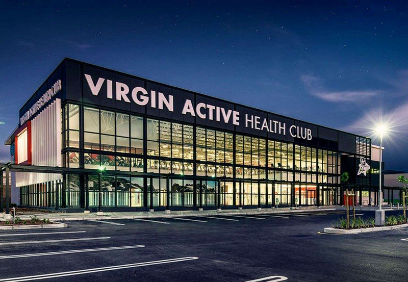 Virgin Active health club exterior with large glass façade illuminated at night.